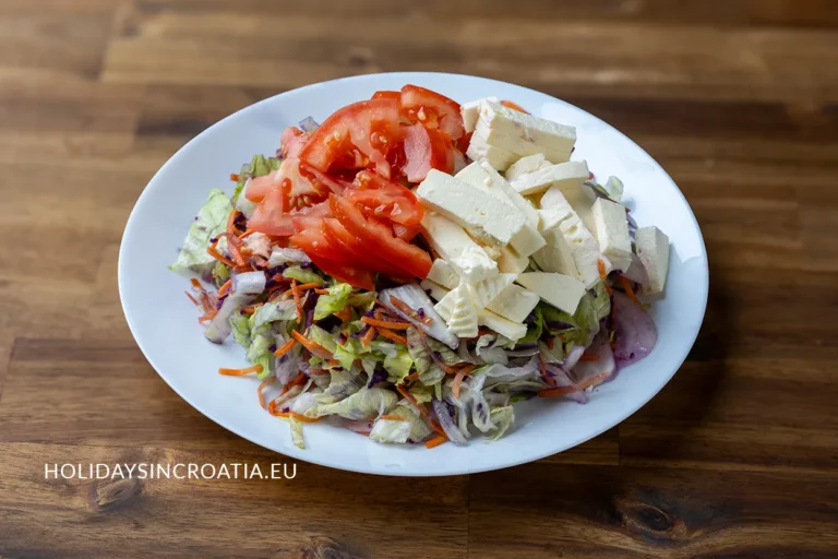 Vegan salad with chopped lettuce, tomatoes, carrots, and dairy-free feta cheese on a white plate, Croatian cuisine.